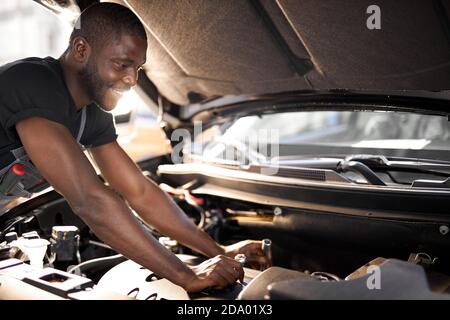 Fröhlich lächelnd afro Mann genießen Reparatur Auto Haube, überprüfen Sie die Details, behebt Maschinenprobleme Stockfoto