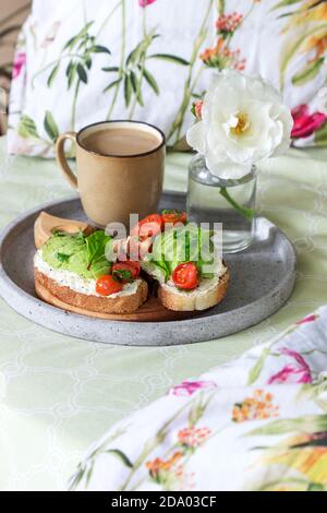 Frühstück mit Sandwiches mit Quark, Avocado und Tomaten und Kaffee, im Bett serviert. Stockfoto