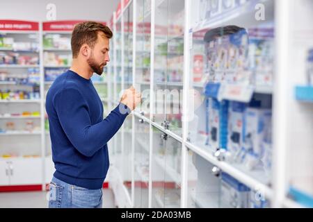Seitenansicht auf gut aussehende kranken Kerl Wahl Pillen, Medikamente in Medizin Regal, er leidet an Krankheit Stockfoto