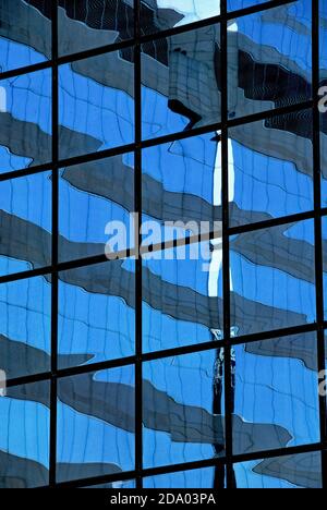 Die Verkleidung eines der Hochhäuser im Central District oder Chung Wan, dem Zentrum der globalen Geschäftsaktivitäten in Hongkong, China, verzerrt die Reflexion eines anderen Firmensitzes in der Nähe mit einem blauen und grauen Welleneffekt innerhalb eines starren schwarzen Rasters. Stockfoto