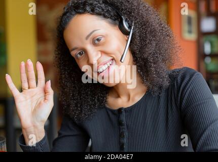 afroamerikanische Frau im Headset mit Online-Gespräch vor dem Laptop-Monitor. Vertikales Foto. Sie schaute auf die Kamera. Stockfoto