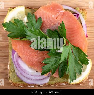 Vollkornbrotscheibe, Avocado-Paste und Lachsscheiben, garniert mit Petersilie und Zitronen- und Zwiebelscheiben. Food Background Konzept. Stockfoto