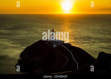 Ein Leuchtturm auf Klippen mit Sonnenuntergang über dem Meer (South Stack Lighthouse, Wales, UK) Stockfoto
