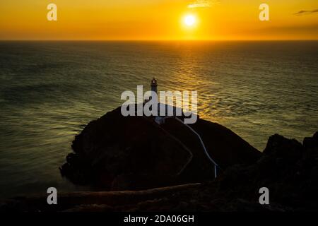 Ein Leuchtturm auf Klippen mit Sonnenuntergang über dem Meer (South Stack Lighthouse, Wales, UK) Stockfoto