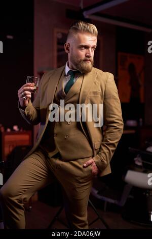 Gut aussehender Mann in Anzug Alkohol trinkend, hält er Glas Getränk in den Händen, posiert allein Stockfoto