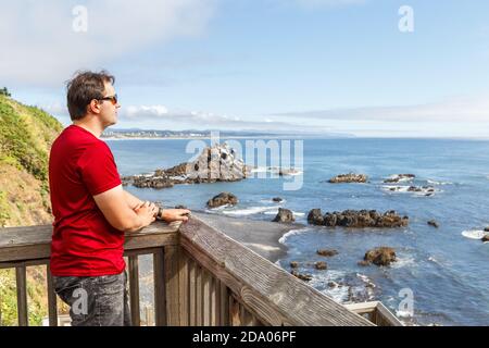 Der junge Mann steht auf der hölzernen Aussichtsplattform und blickt auf das Meer am Cobble Beach unterhalb des Yaquina Head Leuchtturms in Newport, Oregon Stockfoto