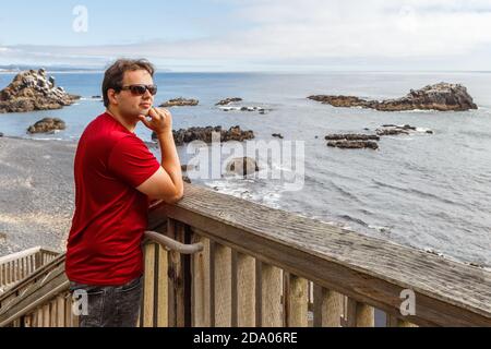 Der junge Mann steht auf der hölzernen Aussichtsplattform am Cobble Beach unterhalb des Yaquina Head Leuchtturms in Newport, Oregon Stockfoto