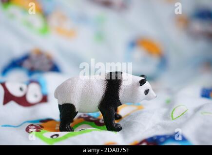 Nahaufnahme eines kleinen Pandas Spielzeug auf einem bunten platziert Stoff mit Eulen auf weißem Hintergrund Stockfoto