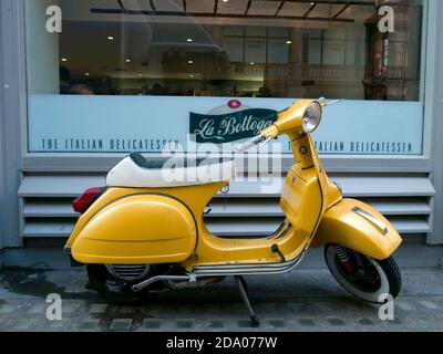 Eine schöne Retro gelbe Vespa geparkt vor einem italienischen Delikatessen, Green Park, London, Großbritannien Stockfoto