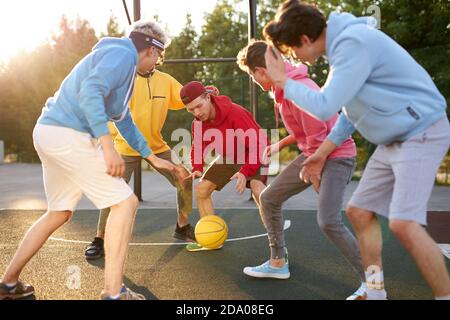 Teenagerjungen spielen Basketball auf dem Spielplatz im Freien und haben Spaß, kaukasischen jungen Jungs dribbeln Basketball mit Freunden blockieren Stockfoto