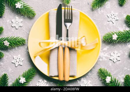 Blick von oben auf das neue Jahr Abendessen auf festliche Zement Hintergrund. Zusammensetzung der Teller, Gabel, Messer, Tannenbaum und Dekorationen. Frohe Weihnachten Konzept. Stockfoto