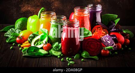 Bunte vegane Gemüsesäfte und Smoothies aus Tomaten, Karotten, Pfeffer, Kohl, Spinat, Rote Bete in Glasflaschen auf rustikalem Küchentisch, ve Stockfoto