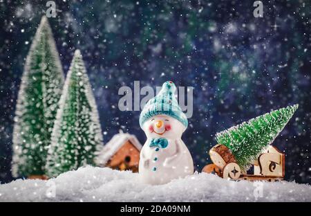 Frohe Weihnachten und fröhliche Neujahrskomposition mit Kopierraum. Kleiner Schneemann trägt Weihnachtsbaum aus dem Märchenwald nach Hause. Winter festliche Backgr Stockfoto