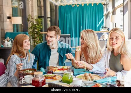 Fröhliche kaukasische Freunde verbringen Zeit zusammen in hellen gemütlichen Zeit Café, sie haben Spaß, reden, chatten. Mittagessen oder sie feiern etwas, unterhaltsam Stockfoto