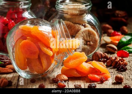 Getrocknete Aprikosen in einem Glas auf dunklem Holzhintergrund mit zerknitterten Nüssen und getrockneten Früchten, selektiver Fokus Stockfoto