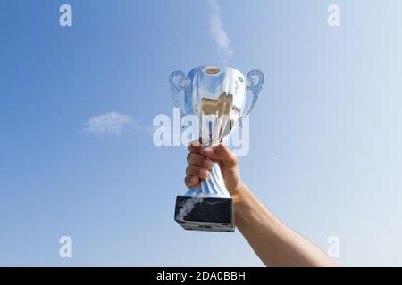 Männlicher Athlet hält einen Pokal hoch. Sieger Athlet zeigt Champion Trophäe Cup auf blauem Himmel Hintergrund. Sport, Leistung, Erfolg c Stockfoto
