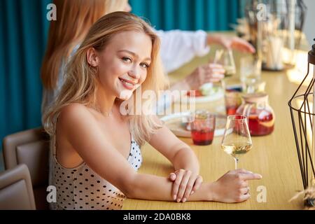 Porträt der kaukasischen Frau mit einem Glas Weißwein im Café oder Restaurant. Junge blonde Frau sitzt posiert, Konzept der Feier, genießen Alkohol, Stil und modischen Lebensstil Stockfoto