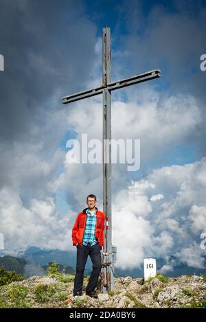 Der männliche Wanderer steht neben dem Gipfelkreuz auf dem Gipfel der Halserspitze in den bayerischen Alpen Stockfoto