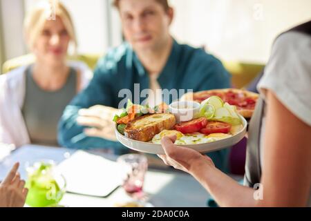 Hand des Kellners serviert Mittagessen im Restaurant, Essen im Restaurant. Kellner in Uniform bei der Arbeit. Salat auf dem Teller Stockfoto