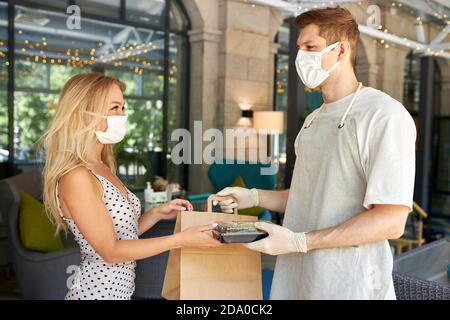 Liebenswert Frau Kunde nehmen ihre Bestellung im Restaurant während Coronavirus, Kellner Personal des Cafés geben Essen in Behälter tragen Schutzhandschuhe, in medizinische Maske Stockfoto