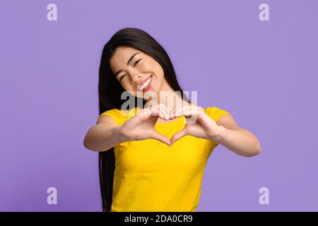 Fröhliche junge koreanische Frau formt Hände wie Herz, zeigt Liebe Geste Stockfoto