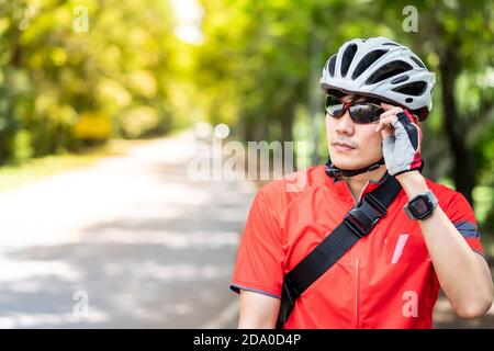Porträt eines asiatischen Radfahrers im Sportswear-Shirt mit seinem Fahrrad in Landstraße mit grünem Baum im Hintergrund. Wochenende Outdoor-Sportler A Stockfoto