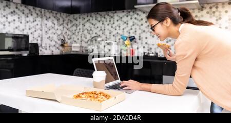 Panorama asiatische Frau arbeiten von zu Hause in der Küche und Essen Lieferung Pizza Essen mitnehmen und Kaffee mitnehmen Während Stadt Absperrung von Coronavirus Stockfoto