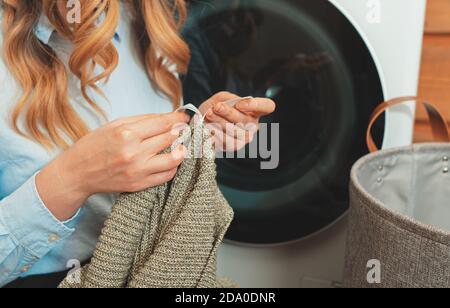 Frau, die den Anhänger auf der Kleidung anschaut, bevor sie die Kleidung in die Waschmaschine einlädt. Stockfoto