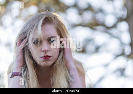 Porträt einer gestressten jungen Frau, die ihren Kopf an beiden Händen hält und die Kamera anschaut. Stockfoto