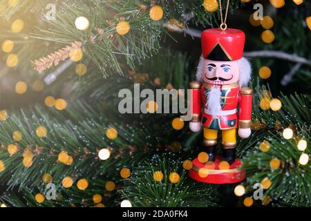 Spielzeug lustige Nussknacker hängen auf Weihnachtsbaum. Neujahr, Feiertagshintergrund mit Platz für Text, Flare und Bokeh Lichter. Weicher, selektiver Fokus. Vorne Stockfoto