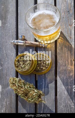 Hochwinkelansicht des Tisches mit Marihuana-Mühle, Marihuana-Knospe, einer Rauchpfeife und einem Glas Bier im Hintergrund. Stockfoto
