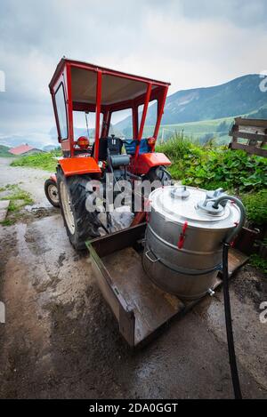 Ein Edelstahlmilchfass wird mit Milch gefüllt auf dem Anhänger eines roten Linder Traktors auf der Ackernalm, Tirol, Österreich Stockfoto