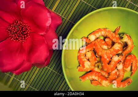 Garnelen in einer tiefgrünen Schale auf der Bambusmatte mit roter Blume. Gebratene Garnelen im asiatischen Stil. Stockfoto