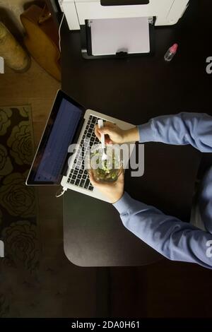 Der Mann hat das Abendessen am Laptop. Salat essen. Von oben gefilmt. Stockfoto