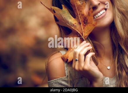 Nahaufnahme Porträt einer hübschen Frau, die ihr Gesicht mit trockenem Ahornblatt bedeckt. Teilfläche. Frohe Herbstferien. Schönheit der Natur Herbst. Stockfoto