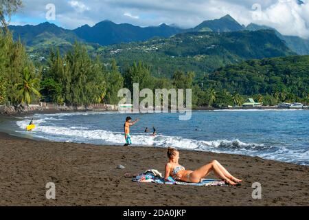 Surfer und Sonnenbaden am Strand mit schwarzem Sand auf Pointe Venus, Tahiti, Französisch-Polynesien, Tahiti Nui, Gesellschaftsinseln, Französisch-Polynesien, Süd-Pa Stockfoto