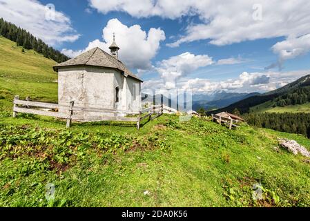 Weiße, mit Schindeldach bedeckte Kapelle auf der Ackernalm Almwiesen vor einem Bergpanorama in Sonnenschein, Tirol, Österreich Stockfoto