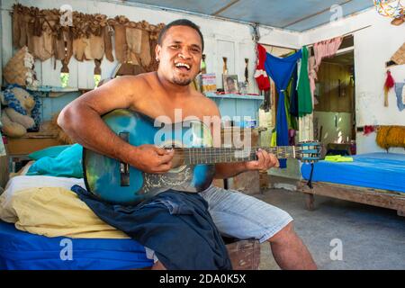 Im Inneren eines traditionellen Hauses in Rangiroa, Tuamotus-Inseln, Französisch-Polynesien, Südpazifik. Mann spielt Gitarre und singt mit seiner Familie. Stockfoto