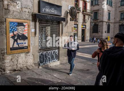 Barcelona, Katalonien, Spanien. November 2020. Ein Mann, der Pizza isst, läuft an den neuen Graffiti vorbei.Street Graffiti-Künstler tvBoy hat ein neues Stück auf der Plaza Sant Jaume gemacht, um Joe Bidens Sieg bei den US-Wahlen zu feiern. Kredit: Paco Freire/SOPA Images/ZUMA Wire/Alamy Live Nachrichten Stockfoto