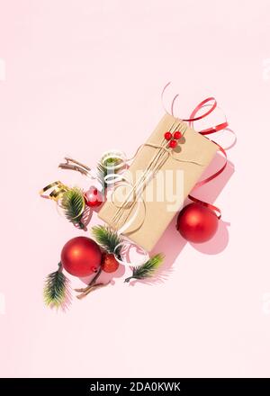 Draufsicht auf Geschenk in Bastelpapier verpackt und gebunden Mit Garn auf rosa Hintergrund mit Weihnachtskugeln und angeordnet Verschiedene Dekorationen Stockfoto