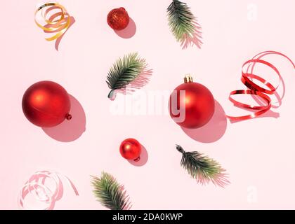Von oben rote Weihnachtskugeln und grüne Fichtenzweige Arrangiert mit glänzenden Bändern auf rosa Hintergrund im Studio Stockfoto