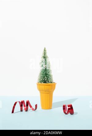 Miniatur-Weihnachtsbaum in dekorativen Eisbecher platziert auf Tisch mit roten glänzenden Bändern im Studio auf blauem Hintergrund Stockfoto