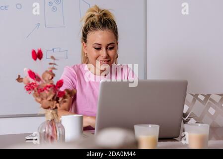 Entzückte Freiberuflerin, die mit einem Laptop am Tisch sitzt und arbeitet Zu Hause aus der Ferne Stockfoto