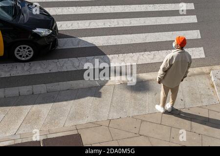 Von oben Ganzkörper männliche Fußgänger tragen lässige Outfit stehen Am Straßenrand in der Nähe des Fußgängerübergangs an sonnigen Tagen Stockfoto