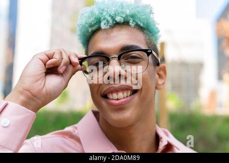 Entzücktes afroamerikanisches Männchen mit gefärbtem blauem Haar und in Stilvolle Brillen stehen auf der Straße und schauen fröhlich auf die Kamera Stockfoto
