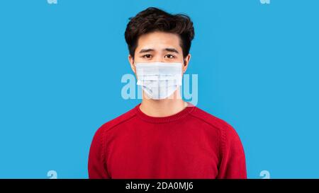 Asian Kerl in medizinische Maske isoliert über blauen Studio Wand Stockfoto