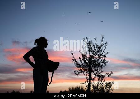 Niedrige Winkel Seitenansicht der Silhouette der anonymen Farmerin Stehen im Garten in ländlicher Umgebung und genießen Sonnenuntergang nach Arbeitstag Stockfoto
