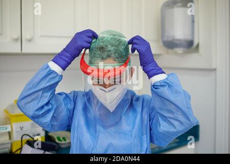 Nicht erkennbare Ärztin in steriler Uniform und Handschuhe anziehen Schutzschild im Krankenhaus beim Blick nach unten Stockfoto