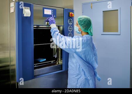Seitenansicht Krankenschwester trägt sterile schützende uniform Druckknöpfe Auf moderner Sterilisationsmaschine während der Arbeit im Krankenhaus Stockfoto
