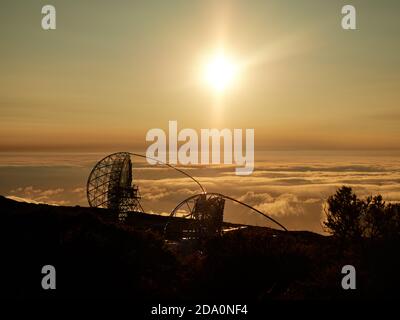 Atemberaubende Sicht auf moderne Teleskope auf dunklem Berggipfel gegen Wolken Und Sonnenlicht während Sonnenuntergang am astronomischen Observatorium auf der Insel Von La Palma Stockfoto